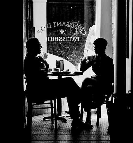 Dos personas tomando café junto a la ventana de una pastelería